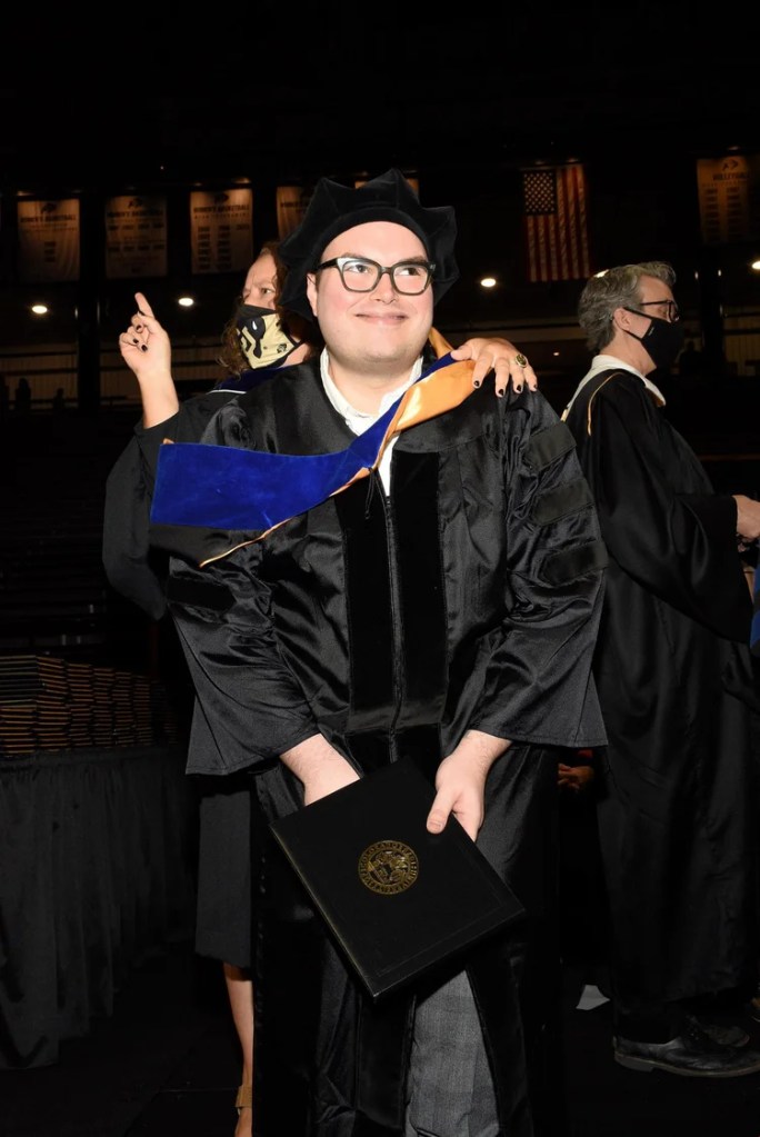 image of m. mason being hooded by p. pezzullo. mason is smiling nad looking off to the right while pezzullo cheers and looks to the left.